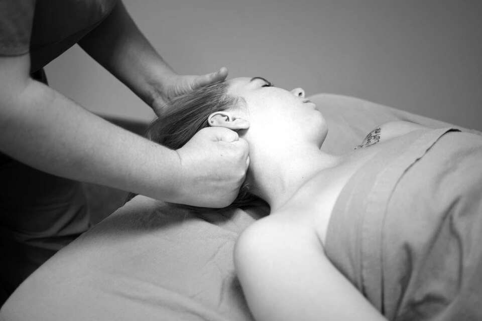 Therapist massaging a client's neck as they lie face-up on a massage table